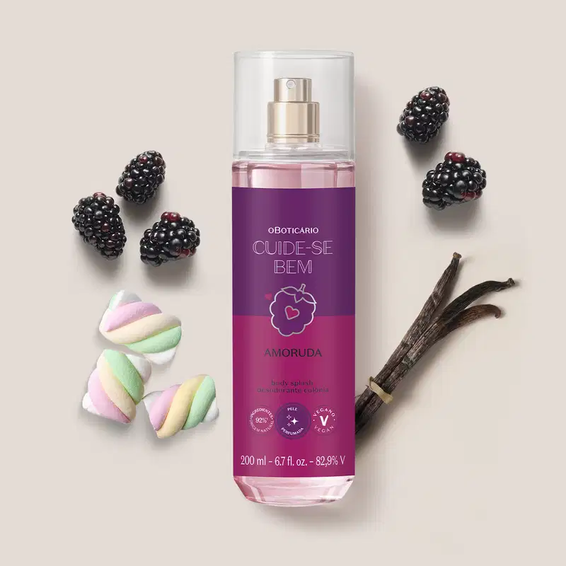 Ambiente de beleza com body splash da marca Cuide-se Bem Amoruda, embalagem roxa com ilustração de amora, rodeado por amoras, marshmallows coloridos e um pedaço de baunilha, sugerindo uma fragrância doce e natural.