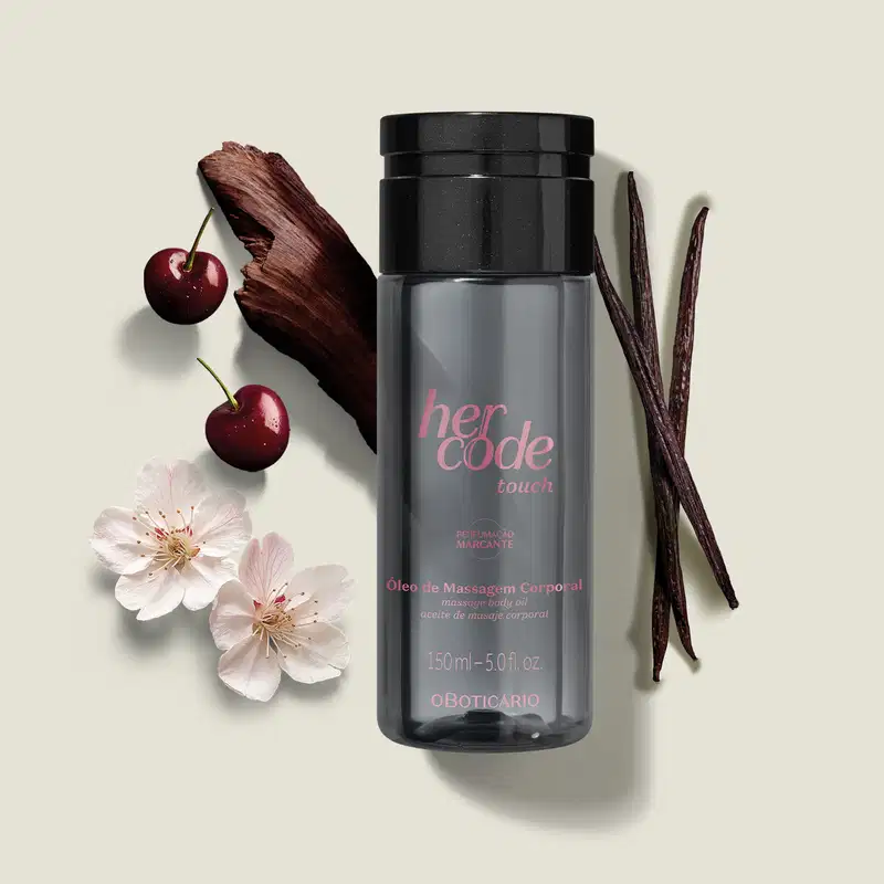 Ao redor do frasco de óleo de massagem corporal Her Code Touch, há flores brancas e cerejas vermelhas, além de um favo de baunilha. A apresentação geral sugere um produto de beleza e cuidados corporais.