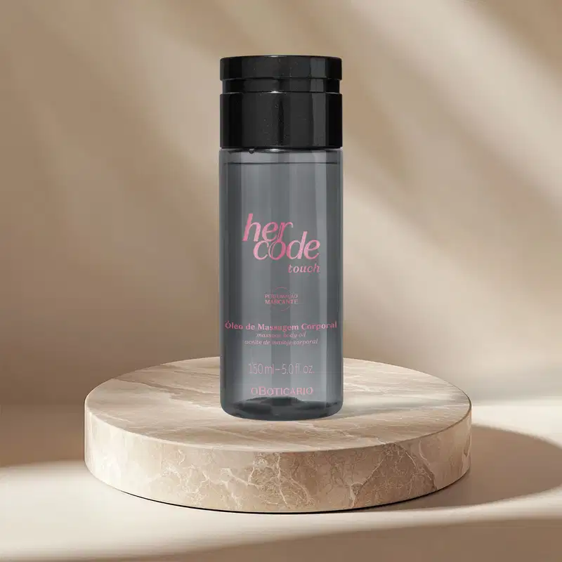 Frasco cinza translúcido com tampa preta e letras douradas de óleo de massagem corporal Her Code Touch sobre superfície de madeira clara, em ambiente com iluminação suave e tons neutros.