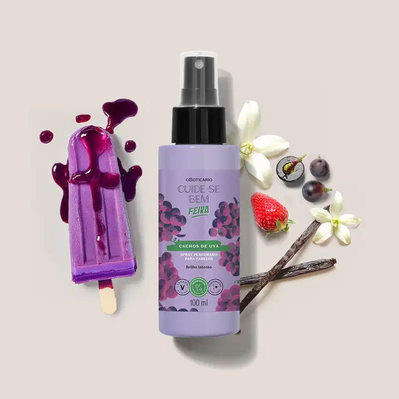 Embalagem de spray perfumado para cabelos Cuide-se Bem Feira Cachos de Uva em meio a flores, frutas e respingos de produto roxo sobre superfície clara.