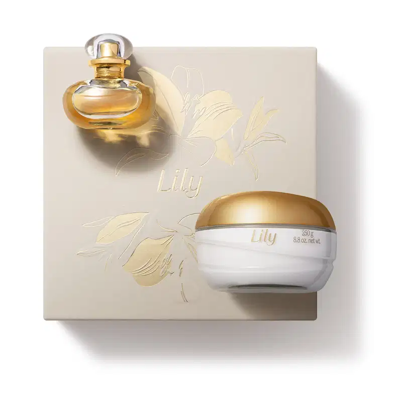 Imagem de uma caixa branca com ilustração dourada de lírios, contendo um frasco elegante com líquido dourado de Eau de Parfum Lily e um pote branco com tampa dourada de creme corporal da mesma marca.