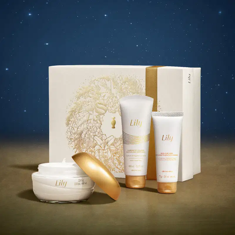 Imagem do Kit Presente Natal Lily com pote de creme hidratante corporal, duas bisnagas, sendo uma de sabonete líquido e outra de geleia corporal e uma caixa presenteável rosa-claro com ilustração floral em cenário com superfície marrom e fundo azul.