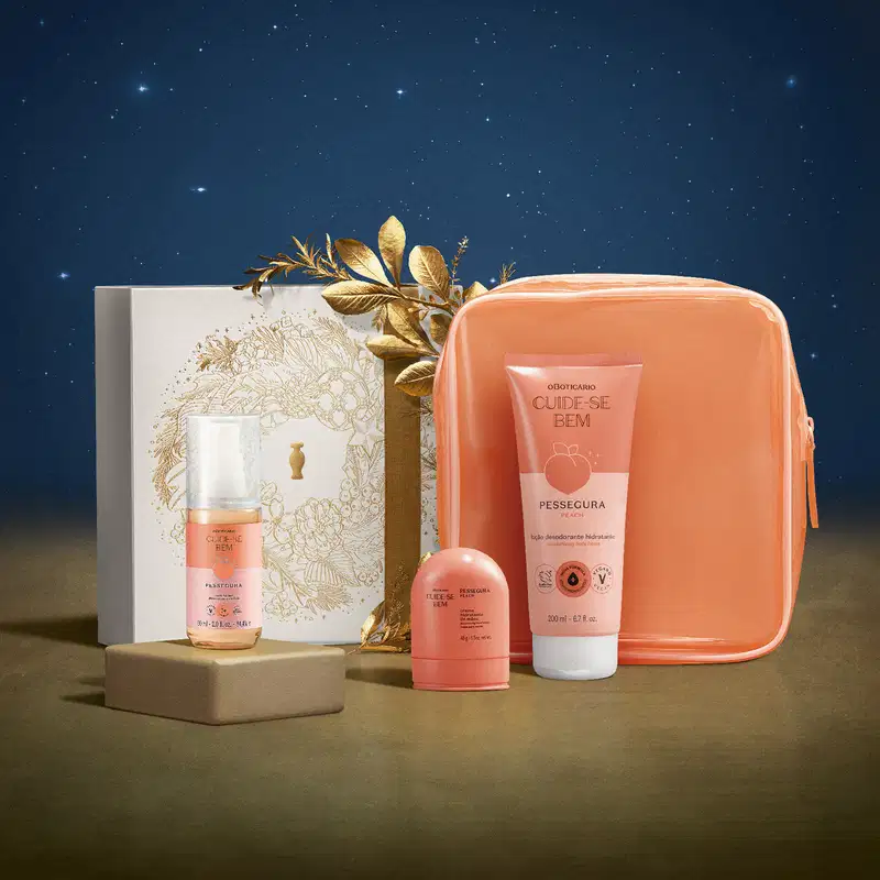 Kit natalino com 4 produtos da marca Cuide-se bem Pessegura e uma caixa de presente branca com detalhes dourados sobre superfície bege e fundo azul escuro estrelado. Folhas douradas adornam a caixa de presente.