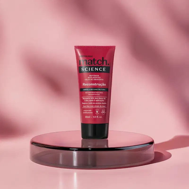 Imagem de tubo vermelho da marca Match Science, posicionado sobre uma superfície reflexiva preta em um ambiente rosa. A binaga contém detalhes em preto e informações impressas em letras brancas.