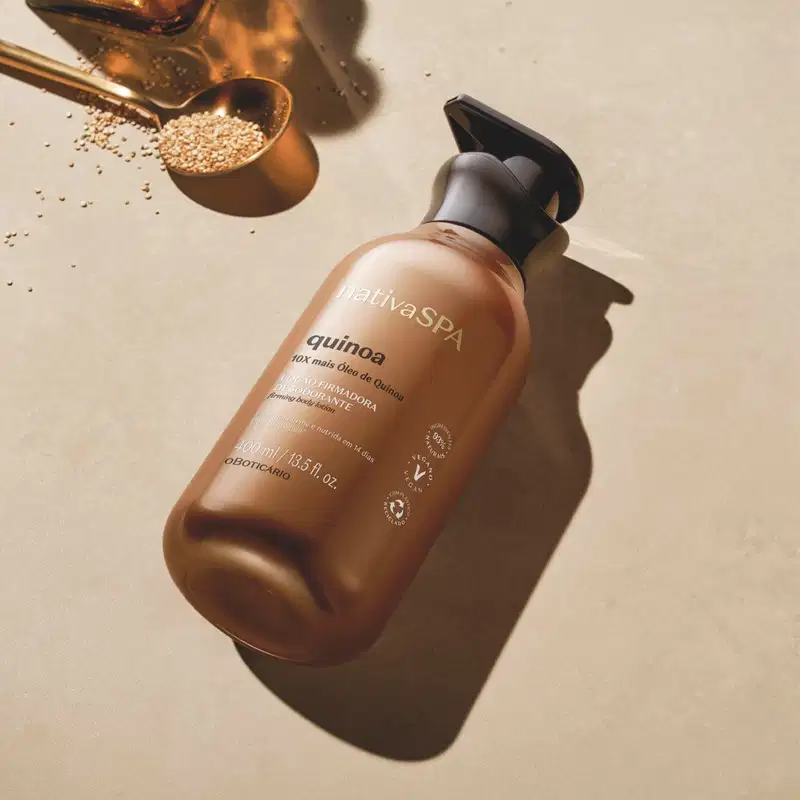 Imagem de um frasco de loção firmadora corporal da marca Nativa SPA Quinoa sobre superfície clara, com colher e grãos de quinoa ao redor, em ambiente iluminado com sombras suaves.