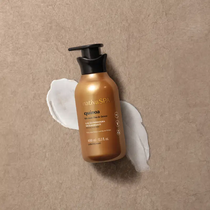 Imagem de um frasco de loção firmadora corporal da marca Nativa SPA Quinoa, com embalagem dourada e tampa preta. Ela está sobre superfície bege com um pouco de creme espalhado embaixo do frasco.