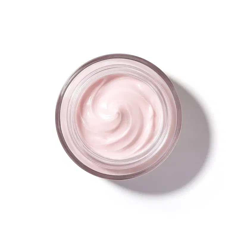 Pote de vidro visto de cima com foco na textura do creme com padrão de espiral suave de textura cremosa e brilhante em tom de rosa claro.