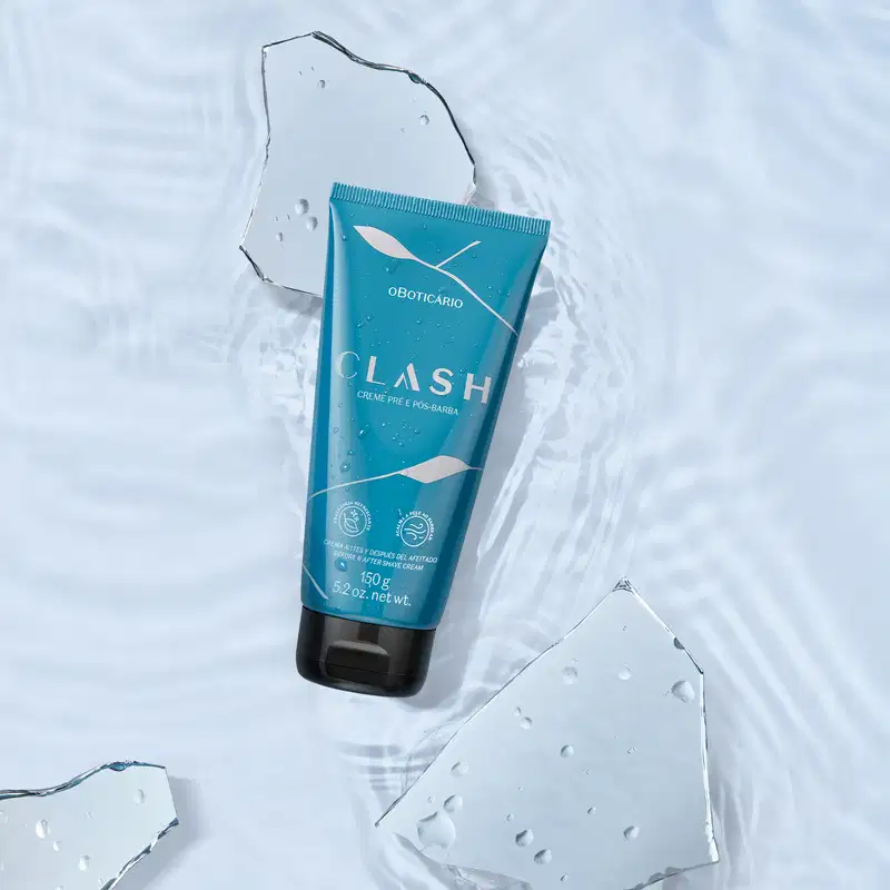 Tubo de creme pré e pós-barba da marca Clash em primeiro plano, flutuando sobre uma superfície aquática com gotas d'água, em uma superfície clara e molhada.