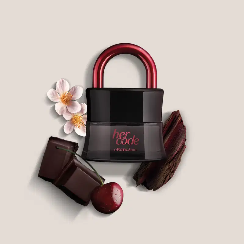 Imagem de um vidro preto com arco rosa metalizado de Eau de Parfum Her Code Clímax, sobre superfície clara com flores, chocolate e madeira ao redor.