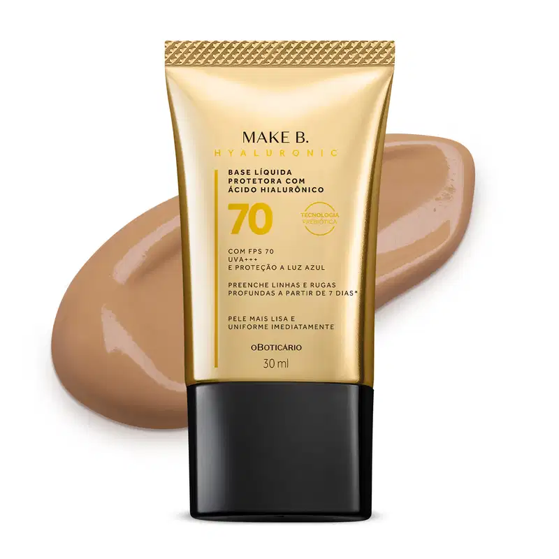 Imagem do tubo de base líquida protetora Make B. Hyaluronic Cor 25. Ele é dourado, possui tampa preta e informações em letras pretas e laranja. Atrás da embalagem está a textura do produto, mostrando sua intensidade e a real cor da base.