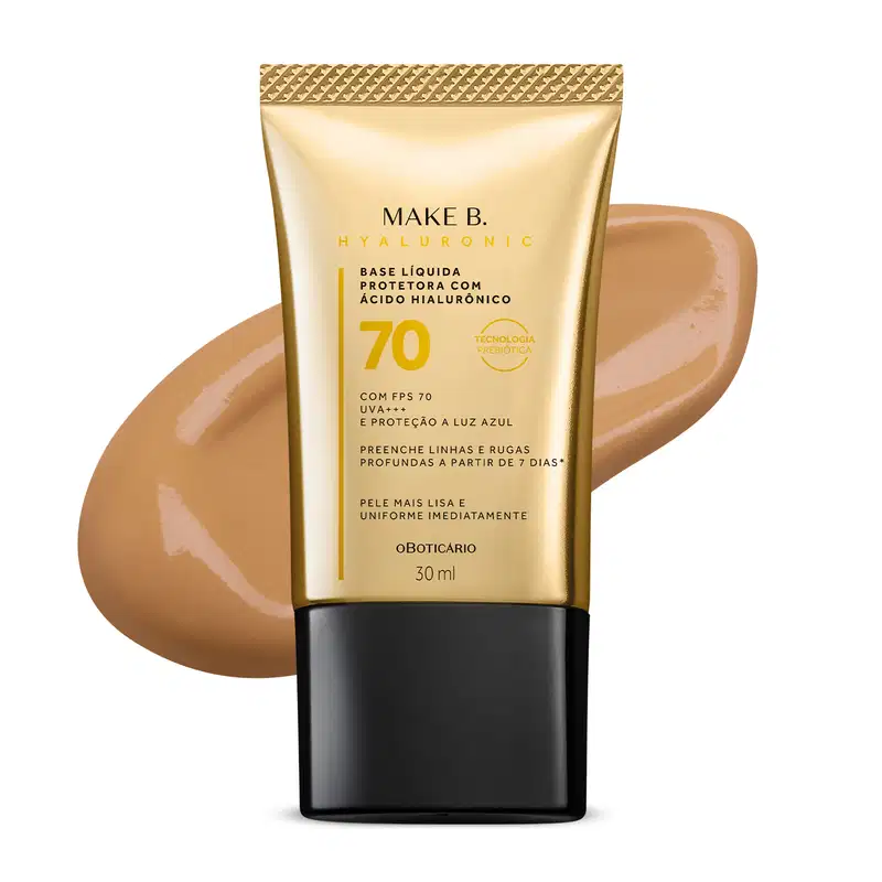 Imagem do tubo de base líquida protetora Make B. Hyaluronic Cor 50. Ele é dourado, possui tampa preta e informações em letras pretas e laranja. Atrás da embalagem está a textura do produto, mostrando sua intensidade e a real cor da base.