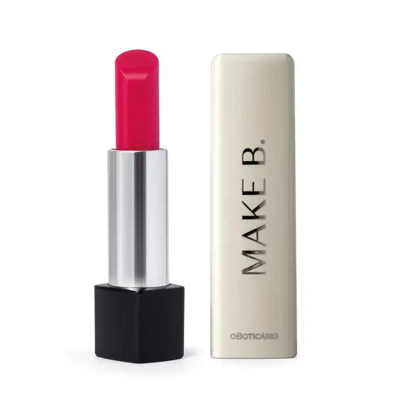 O balm labial rosa da marca Make B. Lip Chronology Color Repair possui uma embalagem preta e prateada com produto  cor de rosa brilhante e tampa branca com a marca gravada em letras pretas.