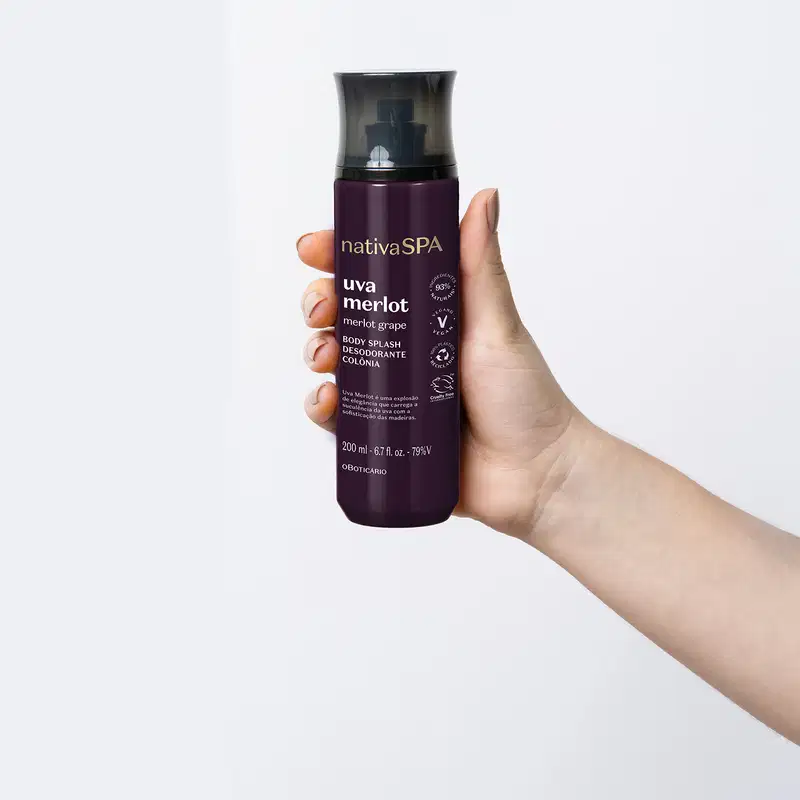 Mão segurando um frasco preto e roxo com letras brancas e douradas contendo loção hidratante corporal Nativa SPA Uva Merlot.