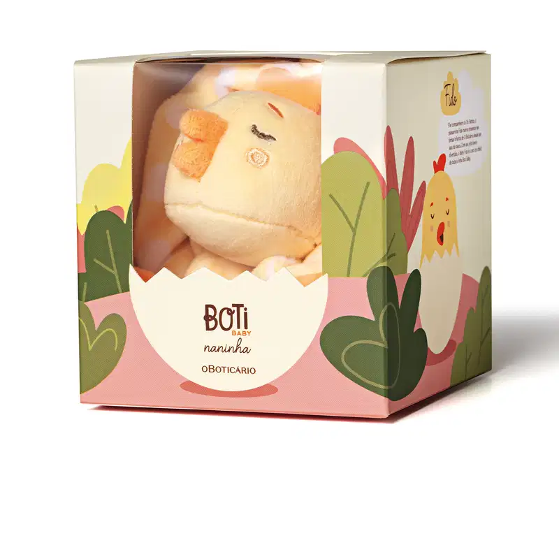 Caixa de papelão com ilustrações coloridas em tons de branco, rosa e verde com uma janela de acetato através da qual se vê um brinquedo de pelúcia em formato de pintinho amarelo dentro.
