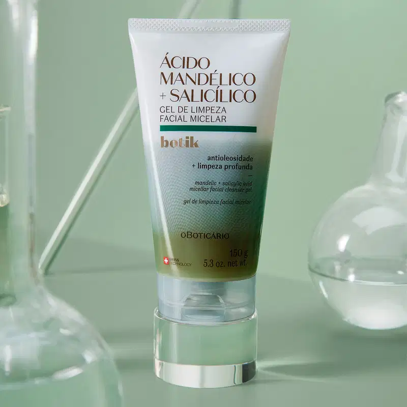Imagem de um tubo de gel de limpeza facial micelar da marca Botik, com ácido mandélico e salicílico, sobre superfície de vidro com reflexos em tons de verde.