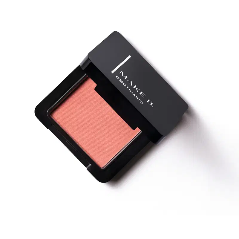 Embalagem preta de blush compacto da marca Make B. aberta, com formato quadrado, e dentro, vemos o produto de tonalidade coral vibrante.