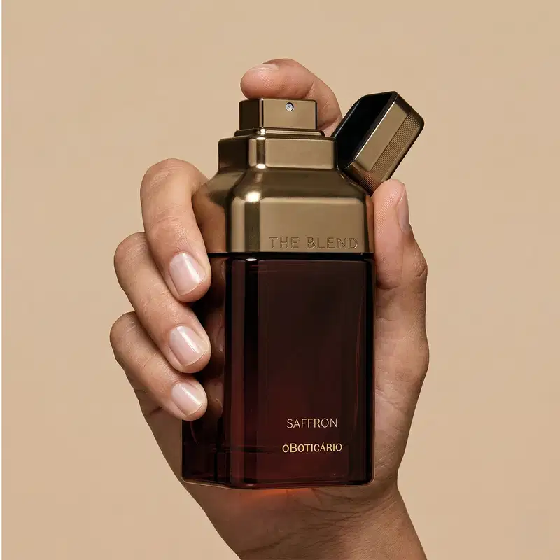 Imagem de uma mão segurando um frasco de fragrância da marca The Blend, com a fragrância Saffron, em um ambiente neutro de fundo bege, destacando o design elegante e sofisticado do produto.