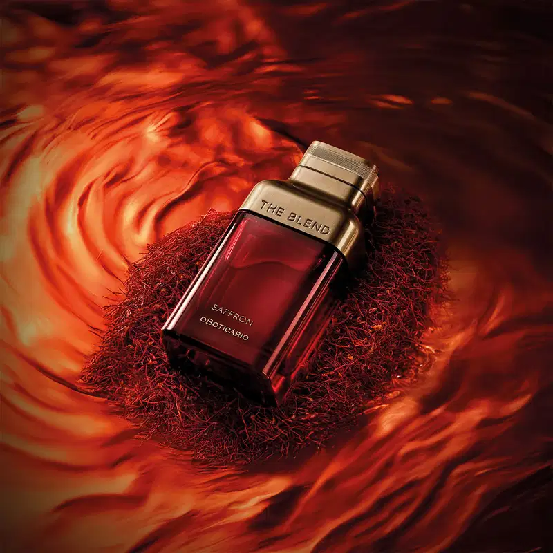Ambiente de luxo e elegância, com um frasco de fragrânciada marca The Blend em destaque, cercado por fios vermelhos que remetem ao aroma de açafrão, sugerindo um produto sofisticado e exclusivo.