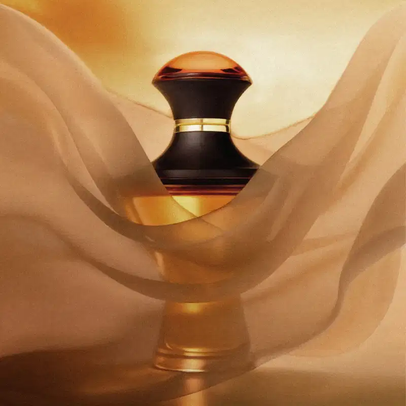 Imagem do frasco de Eau de Parfum da marca Hadiya em preto e marrom com detalhes dourados sobre tecido bege amassado, criando um ambiente suave e aconchegante.