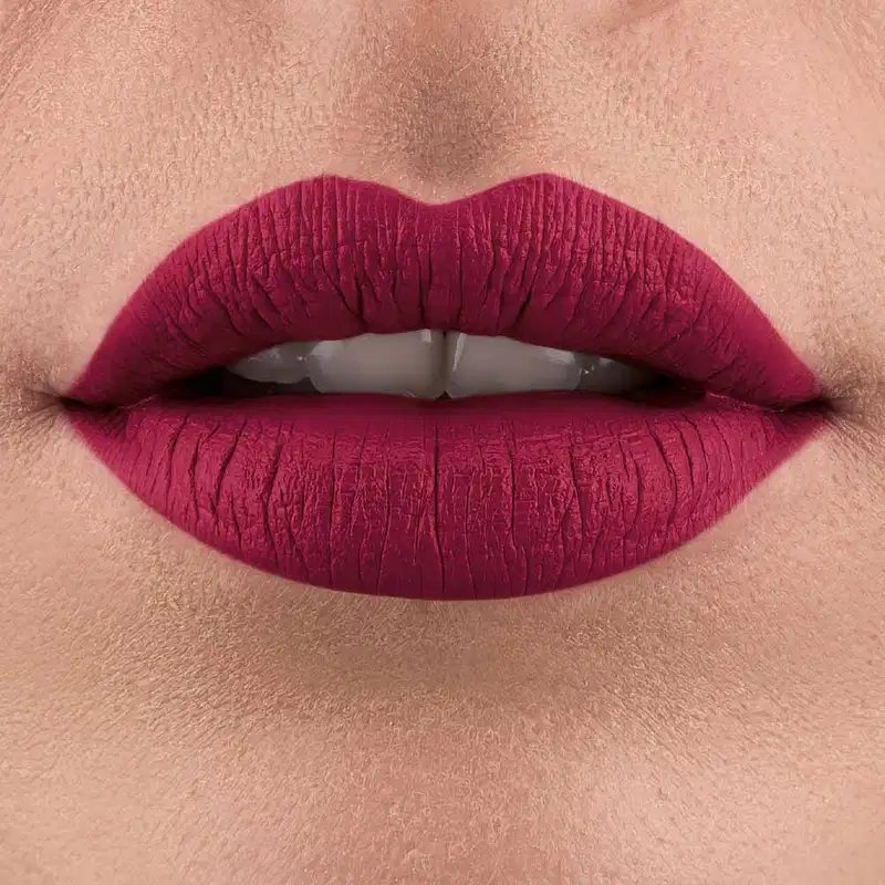 Lábios entreabertos pintados com batom rosa escuro em close-up.  Vê-se um pequeno pedaço de um rosto feminino de pele branca, com destaque para os lábios.