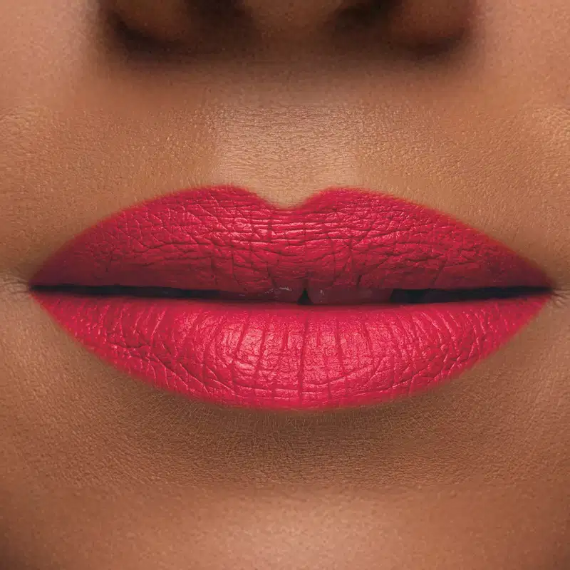 Imagem de um rosto feminino em close-up, evidenciando os lábios com o batom líquido Make B. em tom rosado. A boca está fechada com um leve sorriso.