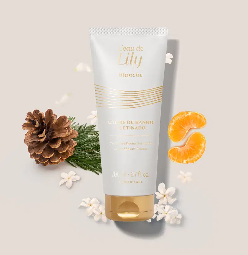 Imagem de um tubo branco e dourado de creme de banho acetinado corporal L’eau de Lily Blanche, com flores brancas, fatias de laranja e pinhas em fundo bege claro.