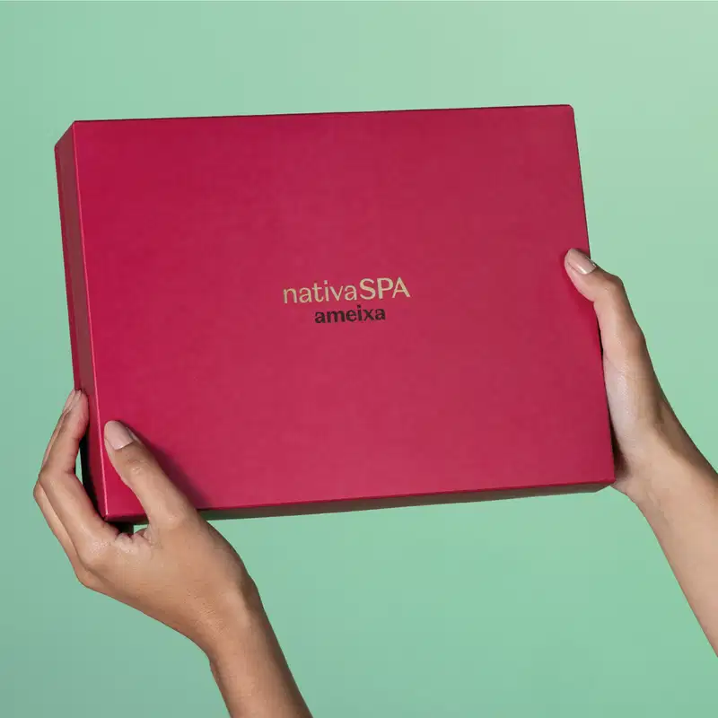 Imagem de uma caixa rosa vibrante com logotipo da marca Nativa SPAA meixa sendo segurada por mãos em fundo verde claro, sugerindo um ambiente  minimalista e neutro.