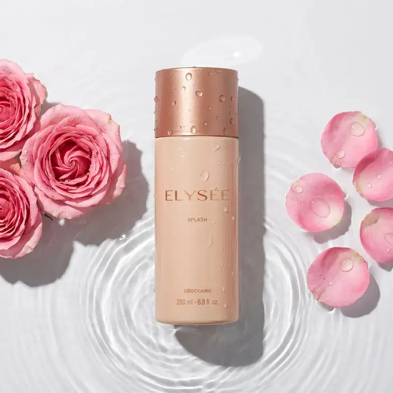 Frasco de item de perfumaria da marca Elysée sobre espelho d'água e com aspecto molhado. Ao redor 3 rosas e suas pétalas espalhadas sobre o espelho d'água, que forma círculos concêntricos denotando movimento.