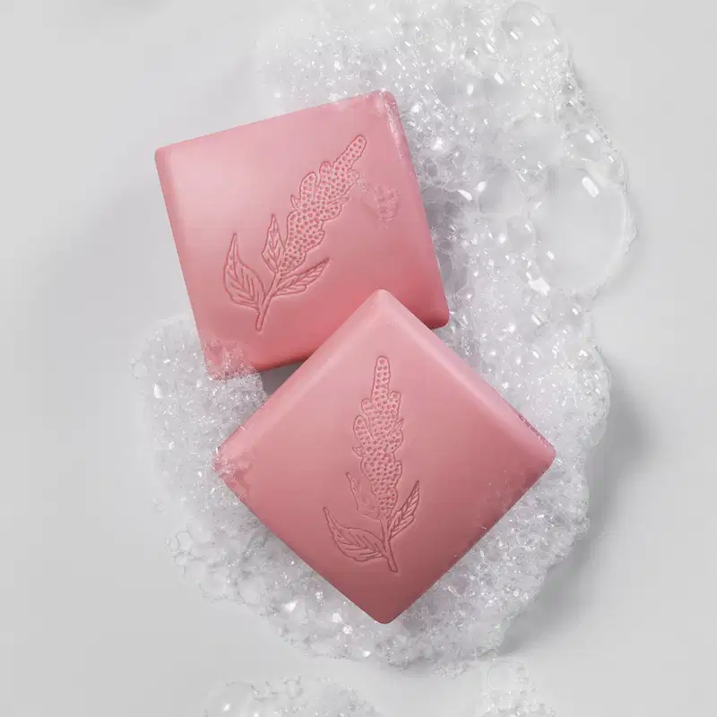 Imagem de dois sabonetes quadrados na cor rosa da marca Nativa SPA Ameixa Plum em superfície molhada com espuma branca ao redor dos sabonetes.