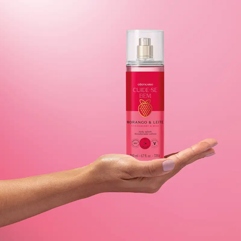 Imagem de um frasco de body splash da marca Cuide-se bem Morango e Leite em mão sobre fundo rosa, em ambiente minimalista e monocromático.