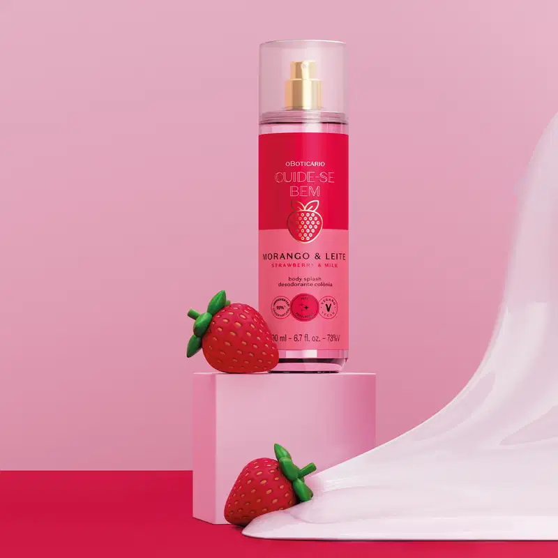 Imagem de frasco de body splash da marca Cuide-se bem Morango e Leite, em fundo rosa e superfície vermelha, com morangos ao lado e creme branco escorrendo.