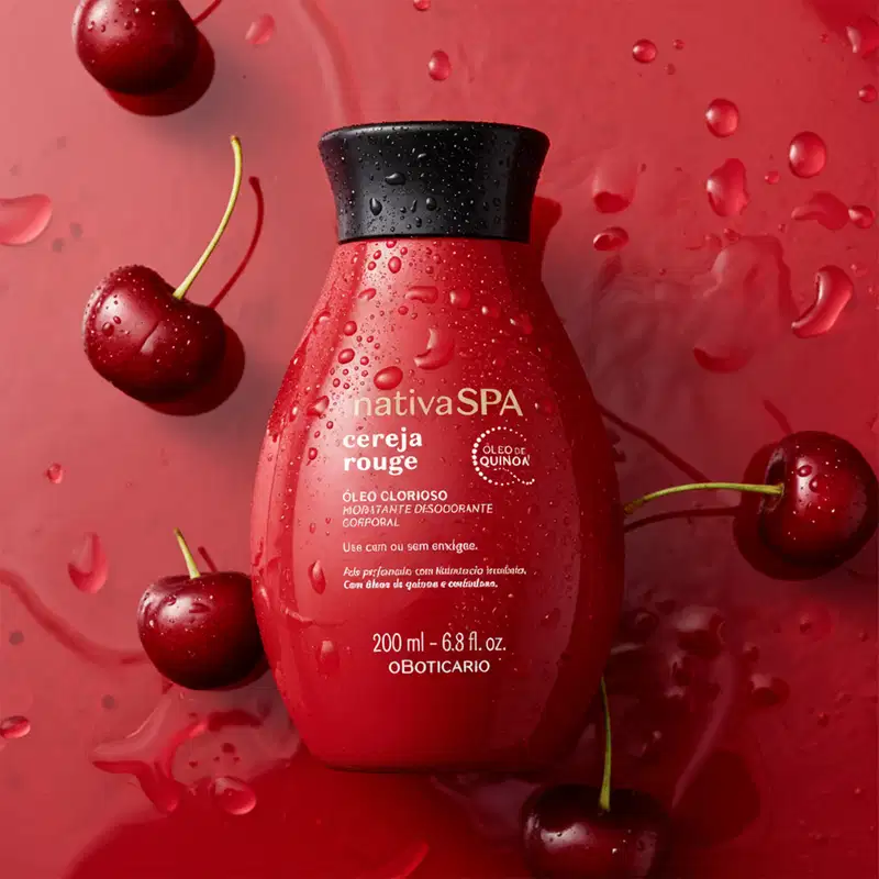 Imagem de frasco vermelho-escuro de óleo glorioso corporal da marca Nativa SPA Cereja Rouge flutuando em água, com fundo em tons de vermelho. Cerejas vermelhas estão espalhadas ao redor do produto.