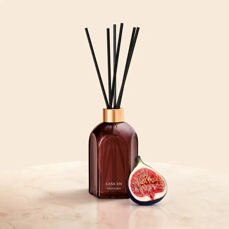 Ambiente de beleza elegante e sofisticado, com um difusor de aromas da marca Casa 214 em um frasco de vidro âmbar e uma fatia de figo fresco, em um cenário minimalista com tons neutros.