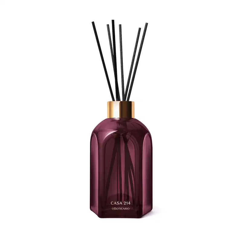 Frasco de difusor de aromas da marca Casa 214, com design geométrico em vidro de cor roxa escura e tampa dourada. Contém varetas de difusão pretas inseridas no frasco.