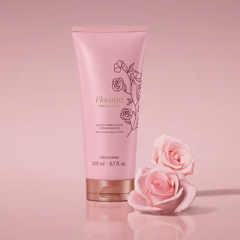 Bisnaga rosa com tampa dourada e ilustrações florais de Loção Hidratante Desodorante Floratta Rose Bouquet em cenário todo cor-de-rosa com duas rosas cor-de-rosa desabrochadas posicionadas ao lado da embalagem.
