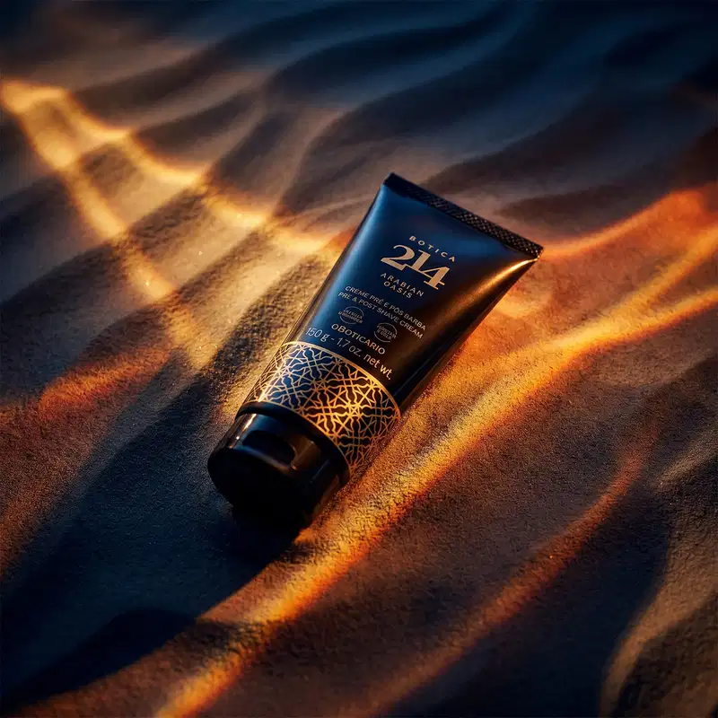 Tubo preto de item de cuidados com a pele pós-barba da linha Botica 214 Arabian Oasis em primeiro plano sobre uma superfície de areia ondulada, com fundo desfocado feixes de luzes douradas que criam um ambiente misterioso e dramático.