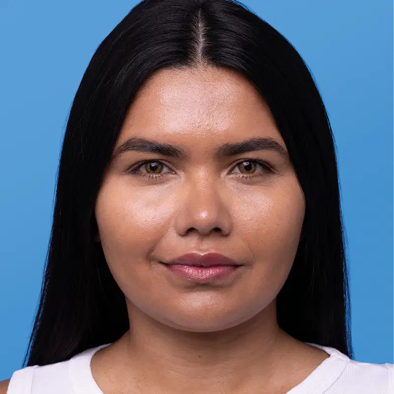Imagem mostra rosto de mulher com cabelo escuro liso e comprido  sobre fundo azul, mostrando o resultado final após uso de protetor solar com cor.
