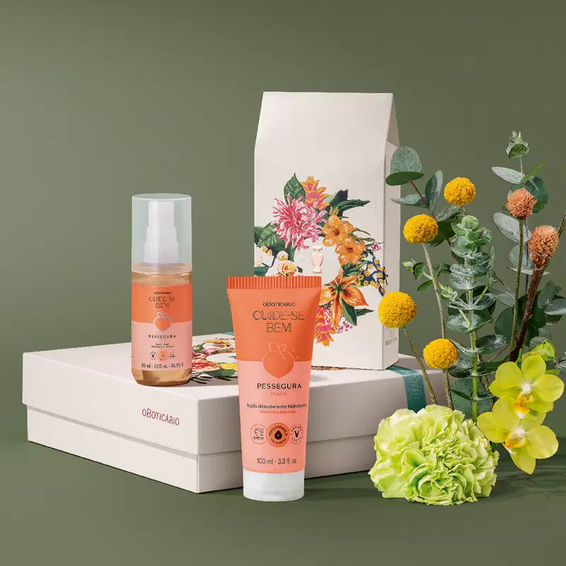 Imagem de kit contendo uma caixa com decoração floral e dois produtos Cuide-se Bem Pessegura, sendo um frasco  spray de body splash  e uma bisnaga de loção hidratante corporal. Ao lado, flores laranjas e amarelas com folhagens sobre superfície verde.
