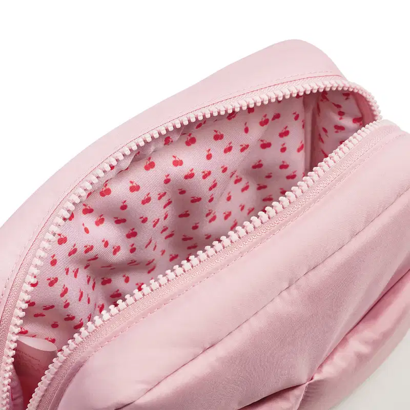 Imagem de nécessaire rosa com zíper, com estampa de cereja vermelha no interior. Sem rótulos ou marcas visíveis. Objeto compacto e portátil.
