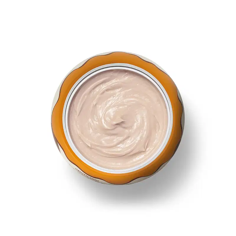 A imagem mostra o recipiente de plástico laranja aberto e contendo um creme branco cremoso e brilhante com textura suave e homogênea.