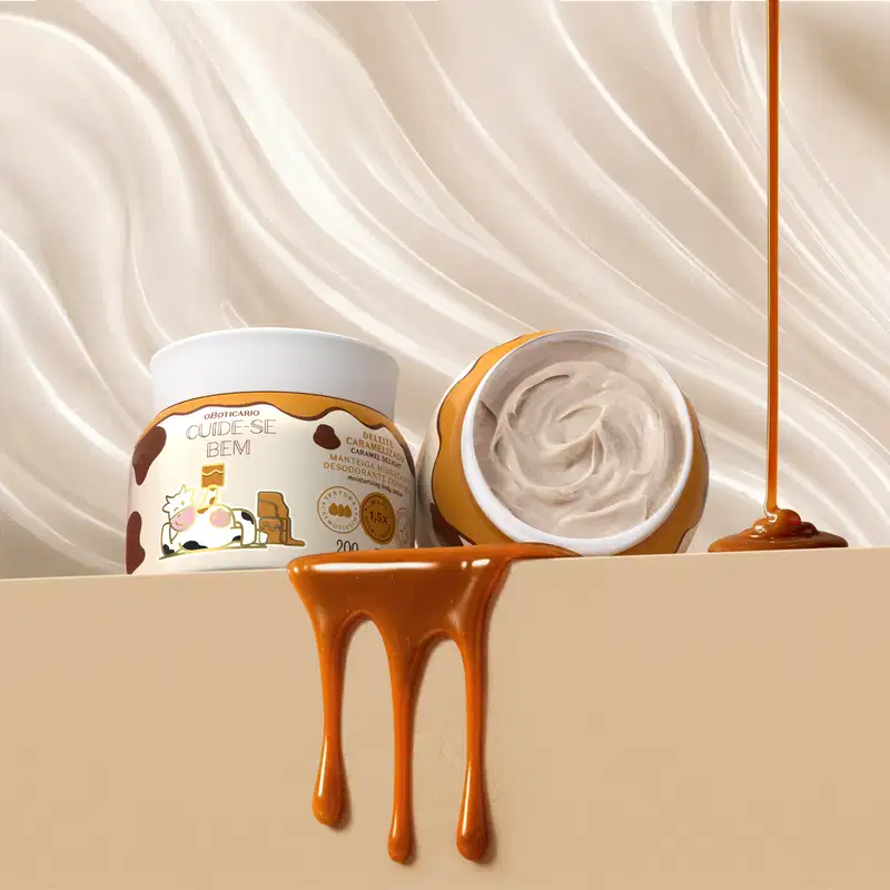O recipiente de manteiga corporal Cuide-se Bem Deleite Caramelizado está aberto e apresenta a textura cremosa do produto. Ao fundo, cortinas brancas onduladas e respingos de doce de leite, trazendo à mente a doçura e aconchego da fragrância.
