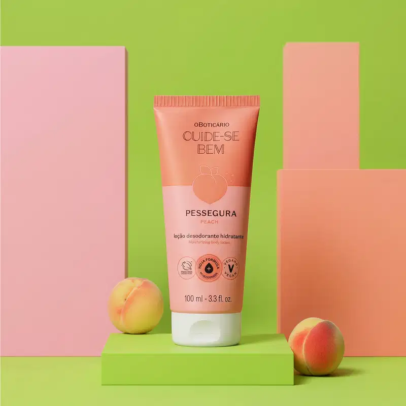 Imagem do tubo de loção corporal da marca Cuide-se Bem Pessegura em embalagem laranja e rosa, sobre superfície verde com lindos pêssegos ao redor, em cenário minimalista e colorido.