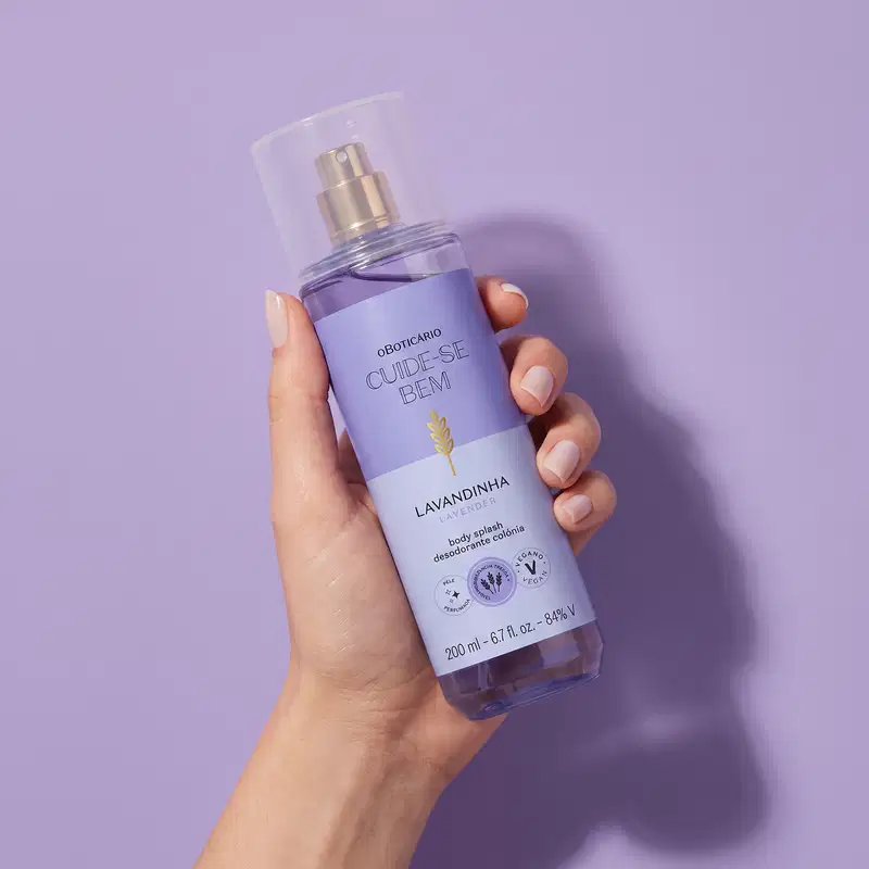 Frasco de item de perfumaria da marca Cuide-se bem, na cor lilás, sendo segurado por mão feminina sobre fundo liso e monocromático na mesma tonalidade.