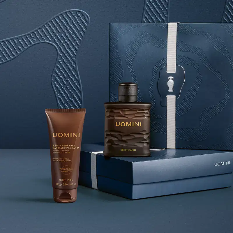 Embalagem e produtos da marca Uomini em ambiente escuro com superfície texturizada, incluindo item de perfumaria, creme para barba e pós-barba, dispostos sobre caixa e acessórios em tons de azul e marrom.