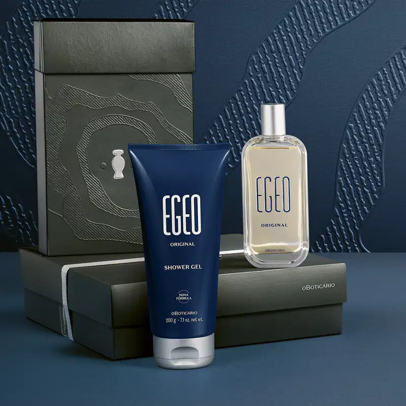 Caixa preta com textura ondulada, tubo de gel de banho e frasco de item de perfumaria da marca Egeo, sobre superfície escura com sombras e reflexos, em ambiente monocromático e minimalista.