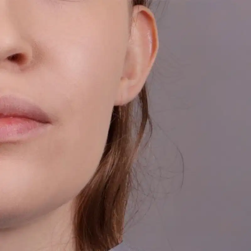 Imagem de close-up do quarto inferior esquerdo de um rosto feminino branco com mecha de cabelo ruivo e comprido aparente em um fundo cinza claro.