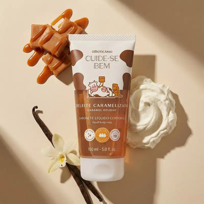 Embalagem branca de sabonete líquido da marca Cuide-se Bem Deleite Caramelizado. Ela posui detalhes em marrom, preto e ilustração de vaca. Ao fundo, flores brancas, doce de leite e favas de baunilha, sugerindo um ambiente relaxante e aconchegante.