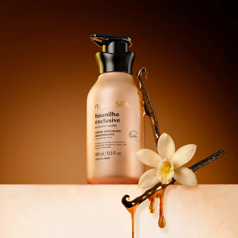 Recipiente de item de corpo e banho Nativa SPA Baunilha Exclusive, com design elegante em tons de dourado e preto. Contém uma flor e hastes de baunilha coberta de caramelo, sugerindo uma fragrância doce e delicada. O ambiente é iluminado em tons quentes.