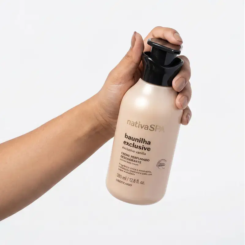 Mão segurando um frasco de item de perfumaria da marca Nativa SPA, com rótulo em inglês "baunilha exclusive". O frasco tem formato cilíndrico, cor bege clara e tampa preta. Fundo branco, com espaço em branco ao redor do produto.