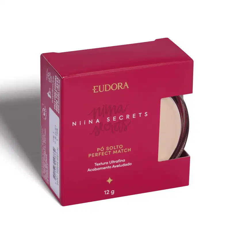 A imagem mostra o produto dentro de uma caixinha rosa escuro, com lateral semi-aberta, que dá pra ver uma parte do produto. A caixa tem logo da marca e linha escrito com letras douradas e branca.